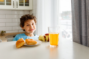Happy kid breakfast with fresh fruits in bright kitchen