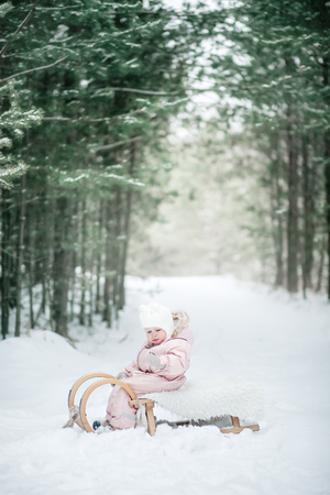 Baby girl with the sled on winter forest