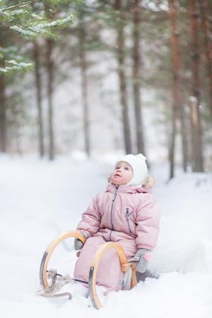Baby girl on the sled in winter forest