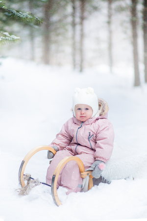 Baby girl on sled in winter forest