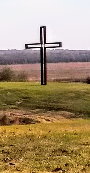A cross that sits on a hillside in the country.
