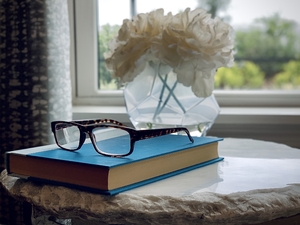 Eyeglasses on a book with flowers in the back in the bedroom