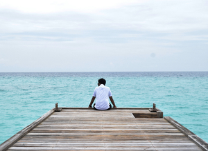 Man sitting on pier with sky and sea background