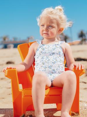 litle girl sitting  on orange chair on beach
