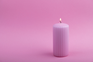 Pink burning candle on pastel pink background